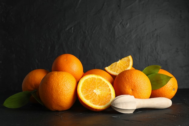 Ripe oranges with wooden juicer on black table against dark background, space for text