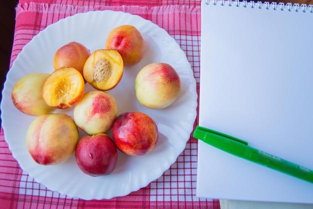 Ripe peaches on a white plate with Notepad and pen