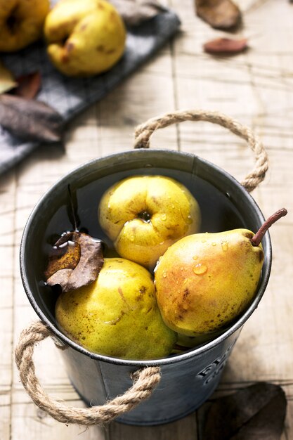 Ripe pears and pear leaves in an iron bucket with water and on a wooden table. Rustic style.