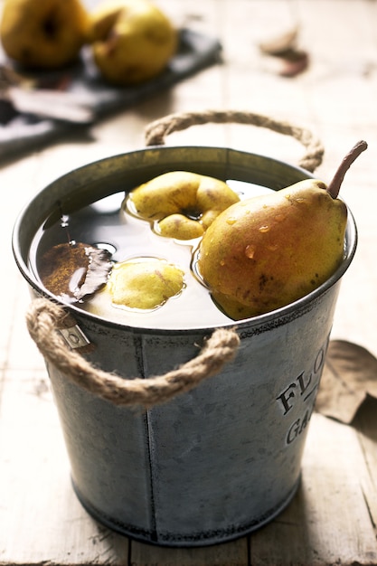 Ripe pears and pear leaves in an iron bucket with water and on a wooden table. Rustic style.