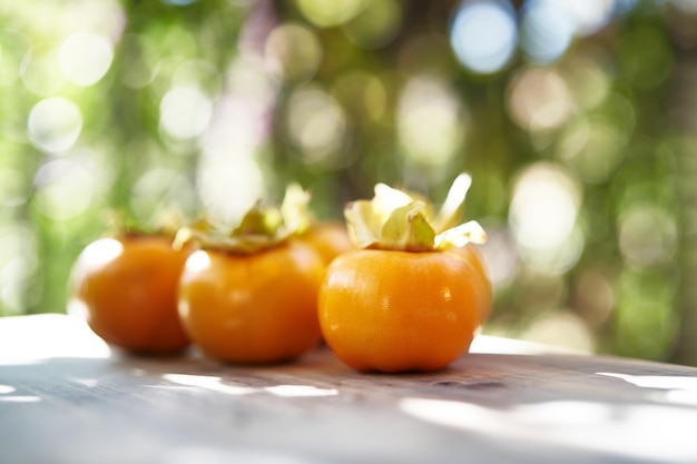 Ripe persimmons lie in a row on a wooden table on a balcony in the sun