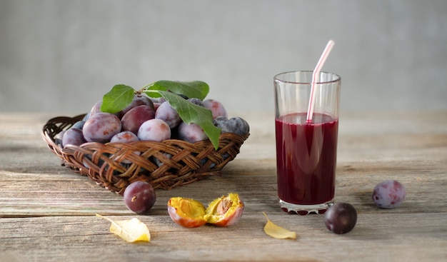 Ripe plums in basket and glass of plum juice