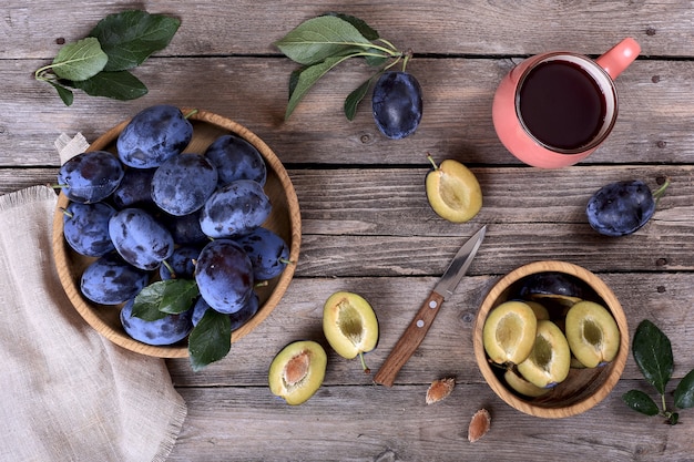 Ripe plums and plum juice on a wooden table, top view