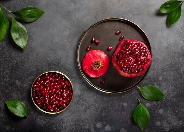 Ripe pomegranate on a plate and peeled pomegranate grain dark surface, close-up, top view