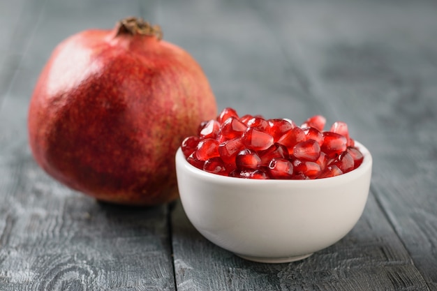 Ripe pomegranate and pomegranate seeds in a white bowl on a black wooden table