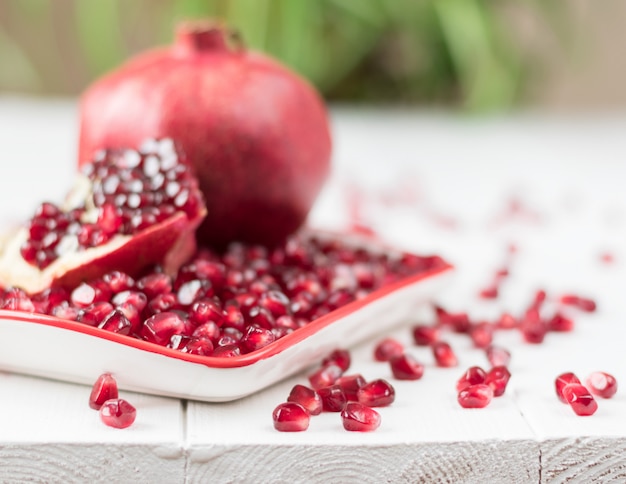 Ripe pomegranate seeds on a white wooden table.