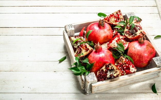 Ripe pomegranates with leaves in the box. On a white wooden table.