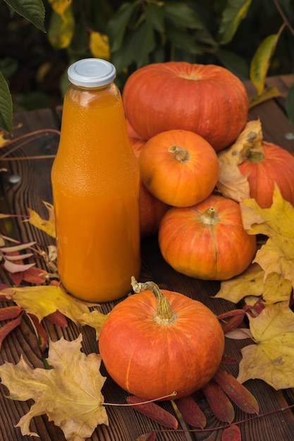 Ripe pumpkin fruits autumn leaves and a bottle of pumpkin juice on a wooden table