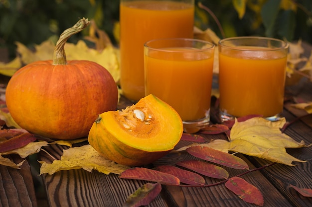 Ripe pumpkins and two glasses of pumpkin juice on a wooden table