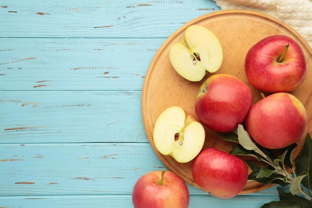 Ripe red apples with green leaves on cutting board on blue wooden background Top view