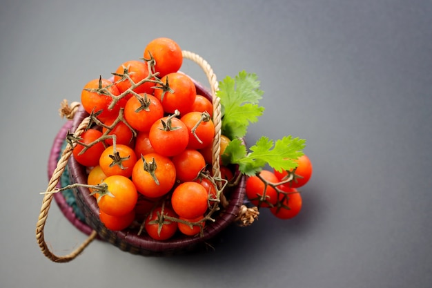 Ripe red cherry tomatoes in a wicker basket on a gray background