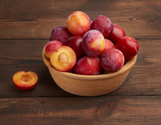 Ripe red plums in a round wooden plate on the table