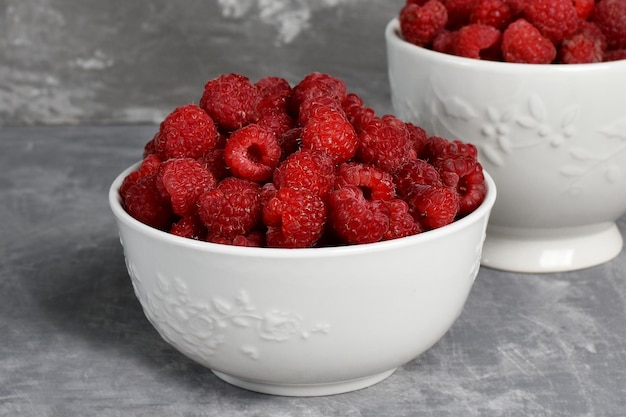 Ripe red raspberries in a white bowl on a stone background berries vitamins harvest