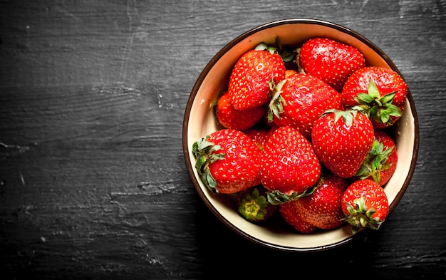 Ripe strawberries in a bowl. On the black wooden table.