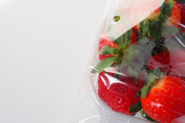 Ripe strawberries in a plastic package on a white background Delicious fresh berries in a container for sale to customers Keeping food fresh Healthy food vitamins and microelements