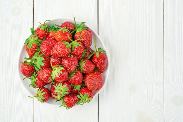 Ripe strawberries in a plate on a white background. Top view, copy space.