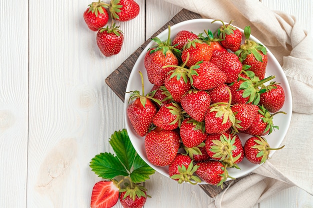 Ripe strawberries in a white plate on a light background