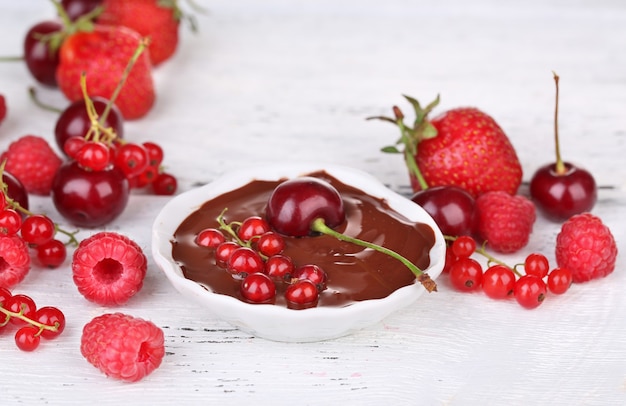 Ripe sweet berries and liquid chocolate on wooden table