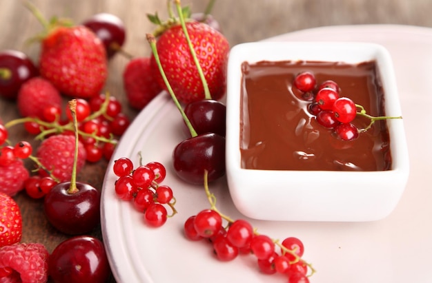 Ripe sweet berries and liquid chocolate on wooden table