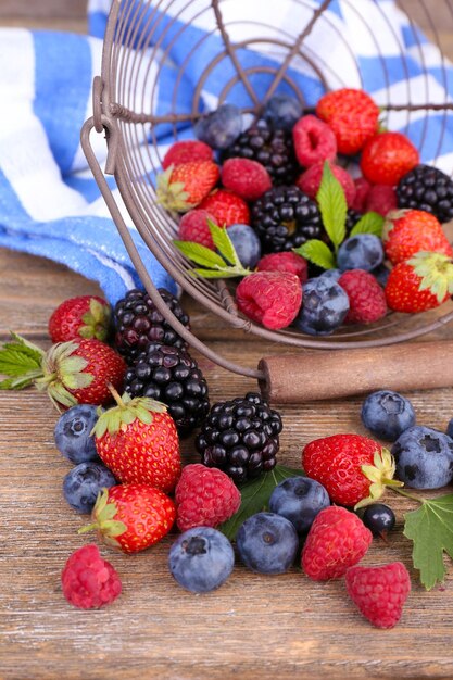 Ripe sweet different berries in metal basket on old wooden table