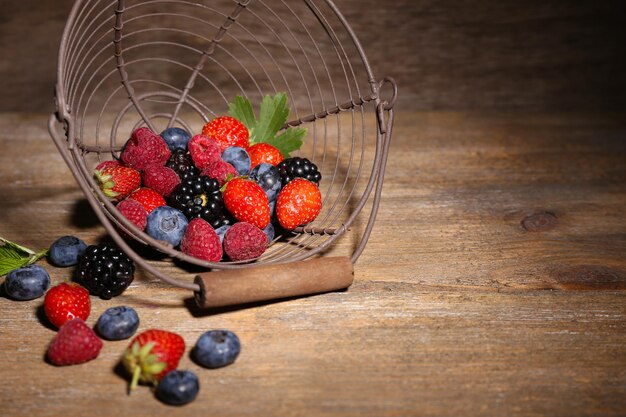 Ripe sweet different berries in metal basket on old wooden table