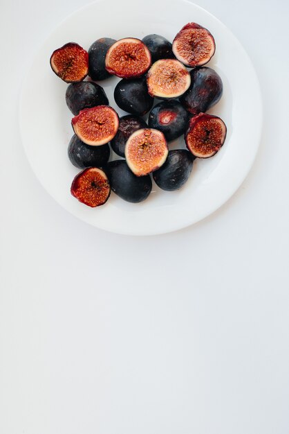 Ripe and sweet figs cut and arranged in a plate on a white background with free space. Fruits and vegetarianism.