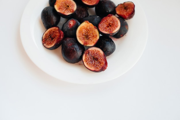 Ripe and sweet figs cut and arranged in a plate on a white background with free space. Fruits and vegetarianism.