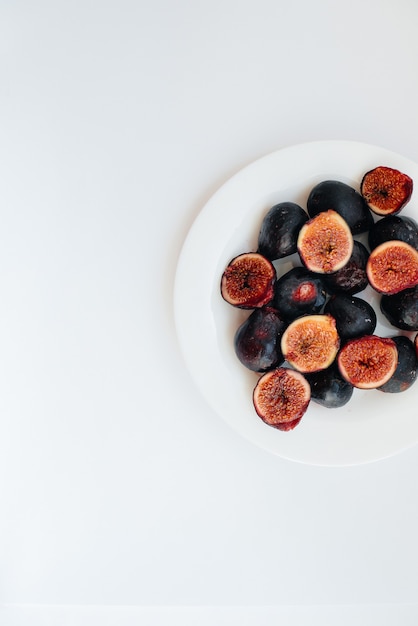 Ripe and sweet figs cut and arranged in a plate on a white surface with free space