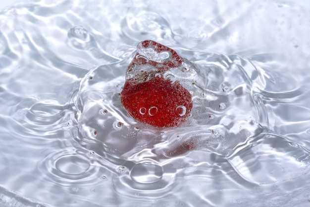 Ripe sweet fresh strawberry is washed in clean cold water with splashes and bubbles close-up