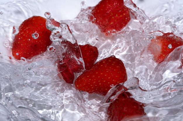 Ripe sweet fresh strawberry is washed in clean cold water with splashes and bubbles close-up