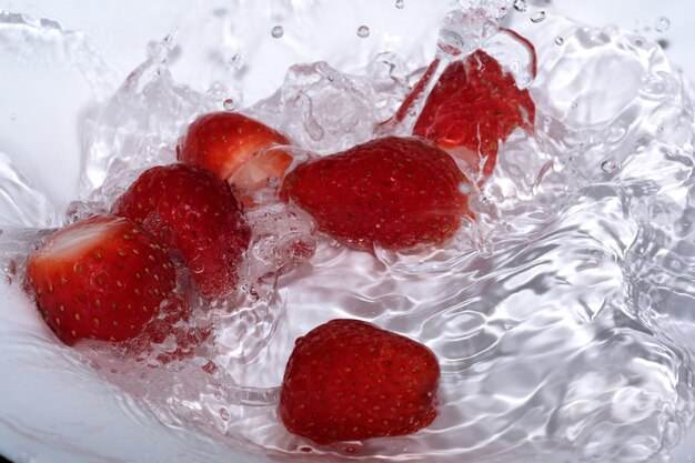 Ripe sweet fresh strawberry is washed in clean cold water with splashes and bubbles close-up