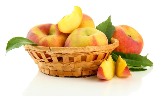 Ripe sweet peaches with leaves in basket isolated on white