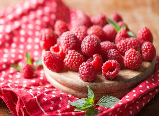 Ripe sweet raspberries in bowl on wooden table.