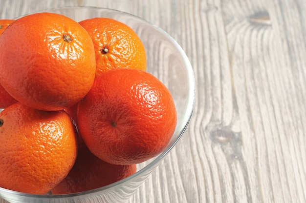 Ripe tangerines in glass bowl on rustic wooden table