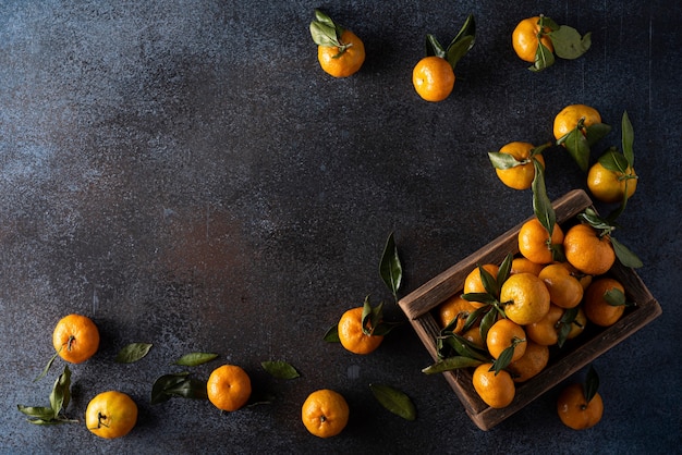 Ripe tangerines with leaves in a wooden box, top view