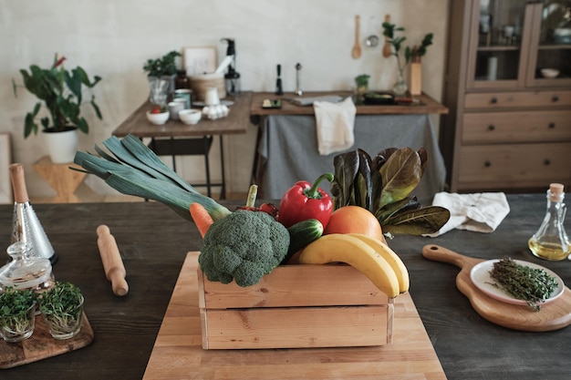 Ripe vegetable and fruit ingredients for dinner in wooden box placed on table with herbs and oil