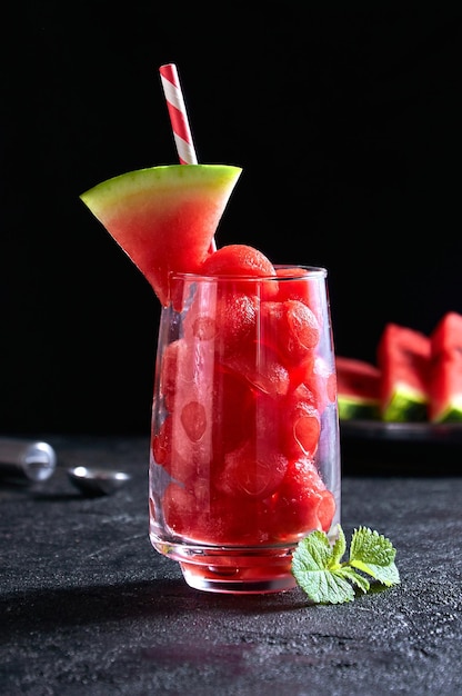 Ripe watermelon noisette balls in glass with mint on dark background Summer dessert