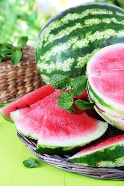 Ripe watermelons on wicker tray on wooden table on nature background