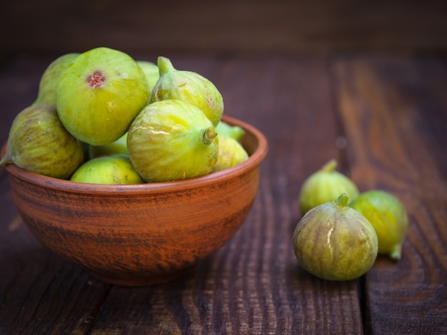 Ripe yellow-green figs in a clay cup on a wooden table