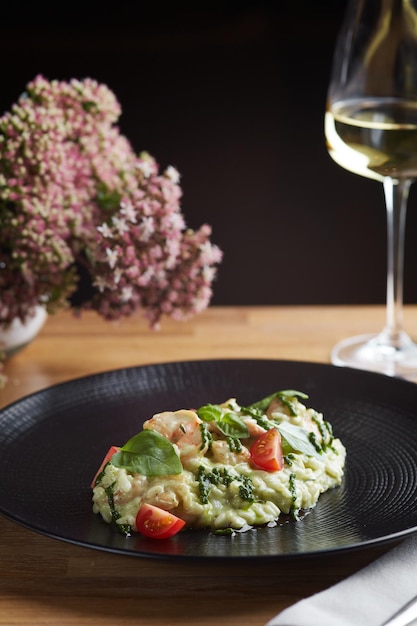 Risotto with pesto basil and cherry tomatoes closeup in black plate on wooden table risotto on wooden table restaurant with glass of wine photo