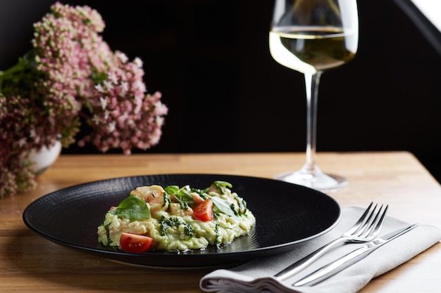 Risotto with pesto basil and cherry tomatoes closeup in black plate on wooden table risotto on wooden table restaurant with glass of wine