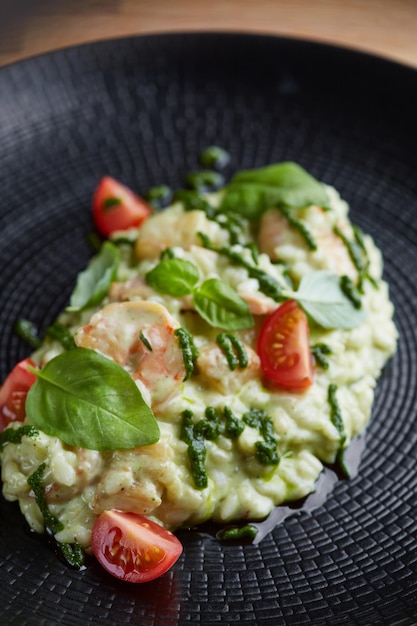 Risotto with pesto basil and cherry tomatoes closeup in black plate on wooden table risotto on wooden table restaurant