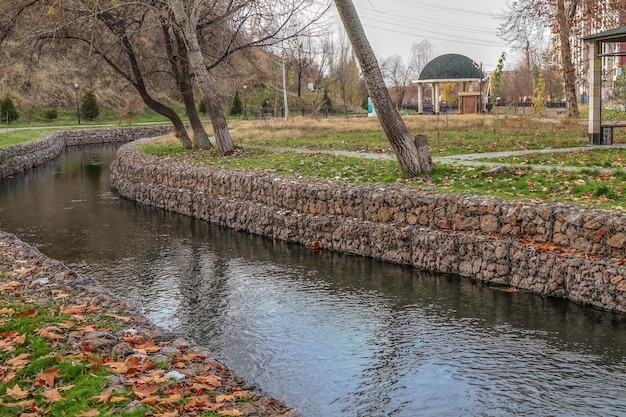 River bank reinforced with stones in a metal grid in the park in autumn