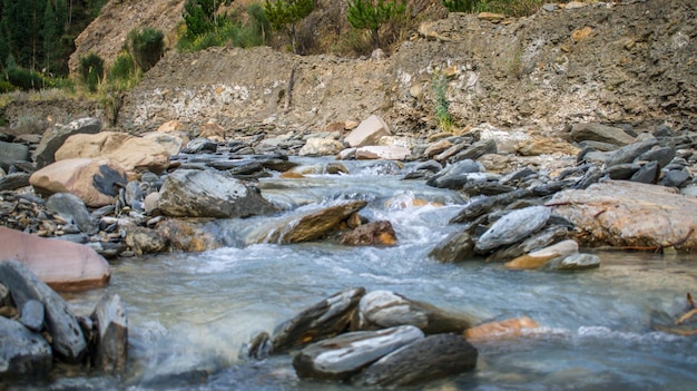 river with rocks in the foreground and bushes in the background, urcospampa, cusco, peru