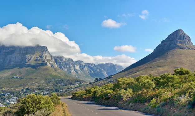 A road along a mountain and green nature with a cloudy blue sky and copy space Beautiful landscape of a peaceful tarred roadway near plants and the wilderness on a summer day