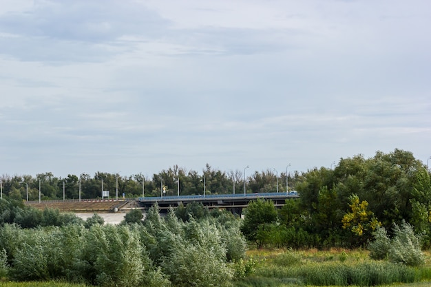 Road bridge passing through a field with trees and bushes. Panorama.