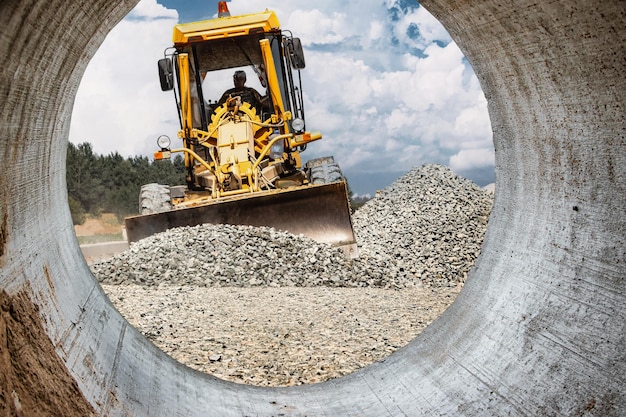 Road grader for land leveling at a construction site Powerful construction machine for ground leveling and excavation Closeup Professional construction equipment View from the big pipe