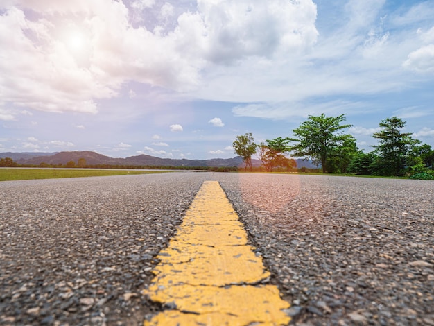 The road leads directly to the mountain view with lawns and trees on both sides There is a wind blowing cloudy sky and sunlight There is a light flare Ghost is a beautiful view and background