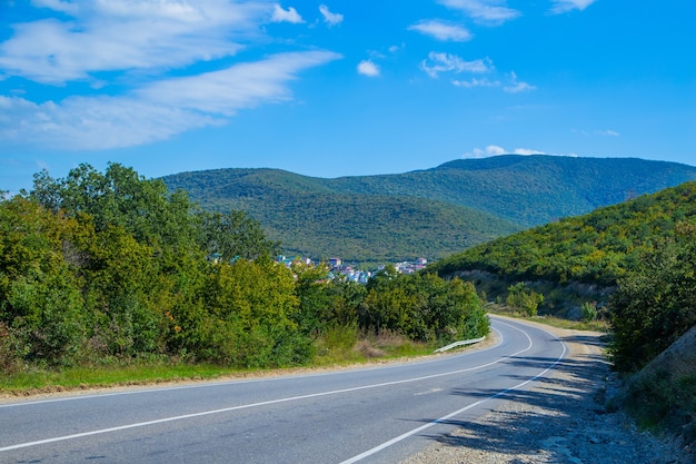 The road in the mountains where green trees grow goes around a bend in the distance you can see a ci...