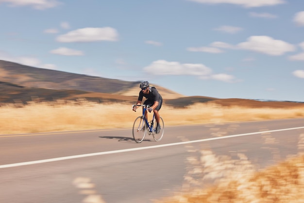 Road nature and man cycling fast for workout exercise and scenic mountain path with motion Health wellness and cyclist on speed bike for morning training practice and bicycle race with blue sky